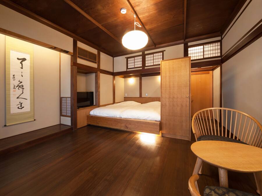 A traditional Japanese-style room with tatami flooring, a low wooden bed, a wooden chair, and a hanging shoji screen.