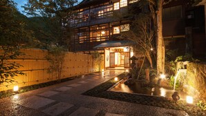 A traditional Japanese building with a wooden exterior, a stone pathway leading to the entrance, and a small water feature in the garden. - KANSUIRO Annex (Hakone)
