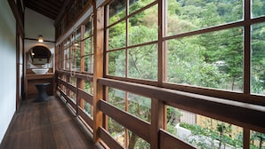 A wooden balcony with large windows overlooking a forested area. - KANSUIRO Annex (Hakone)