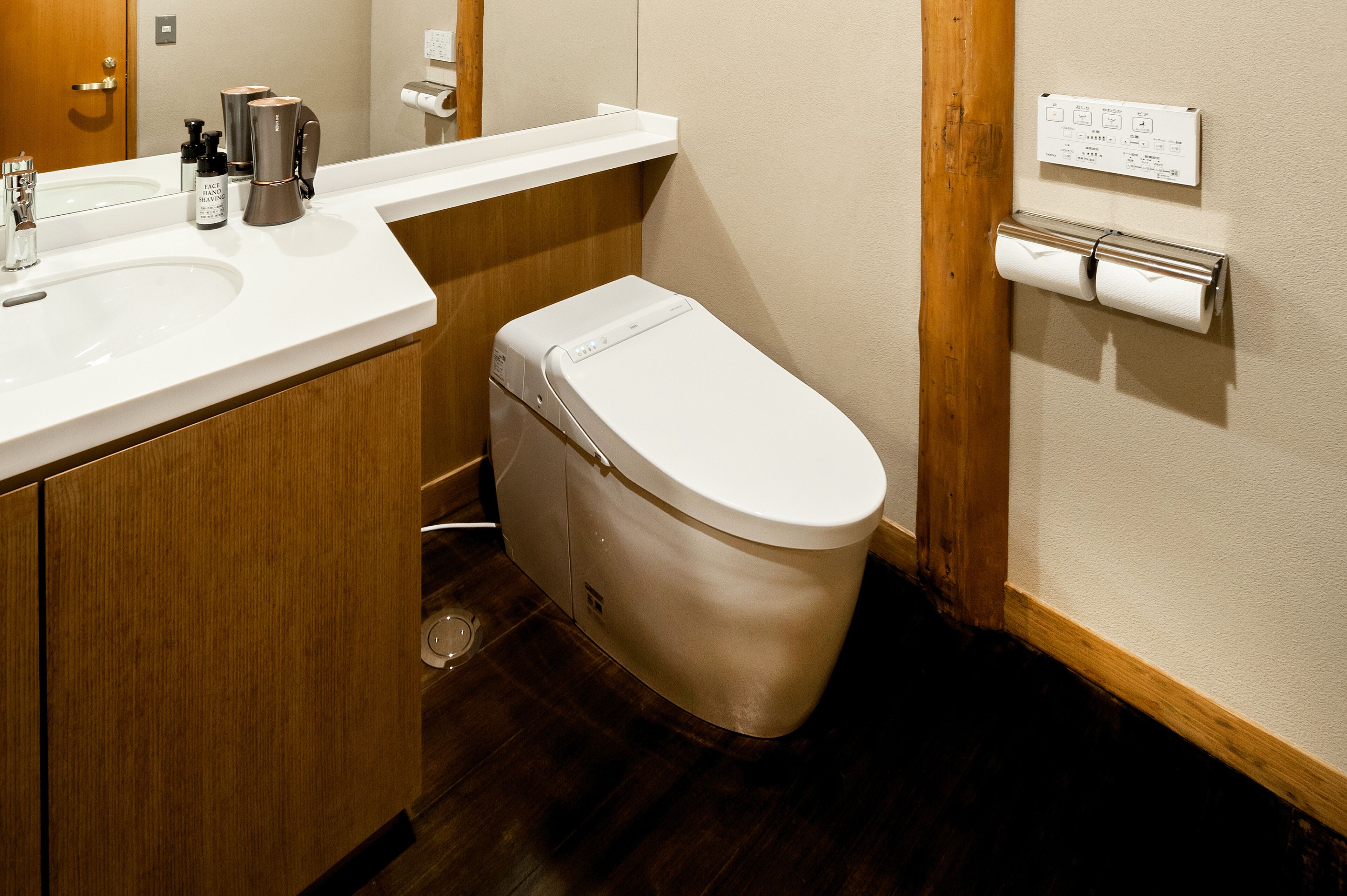 A bathroom with a white toilet, wooden vanity, and a mirror.