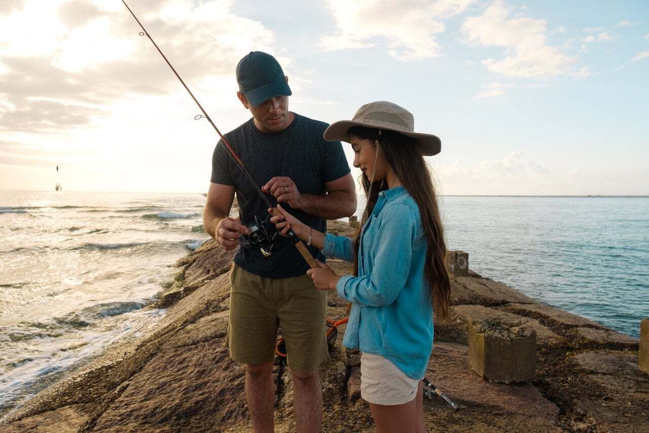 Una pareja pescan cerca del mar, con un muelle rocoso al fondo.