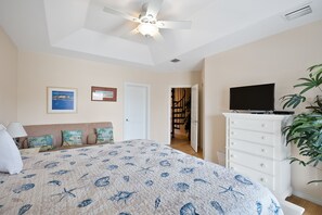 A bedroom with a bed, a ceiling fan, a TV, a dresser, and a plant.