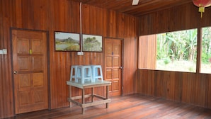 Ein Zimmer aus Holz mit Tisch, Stühlen, Holztüren und einem Fenster mit Blick ins Grüne.