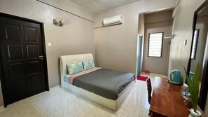 Ein Schlafzimmer mit Bett, einem Holztisch, einer Topfpflanze, einer Klimaanlage und einer Tür.