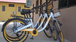 Ein Tandemfahrrad mit Korb und einem Anhänger, geparkt an einem Gebäude mit rotem Dach und gelben Wänden.