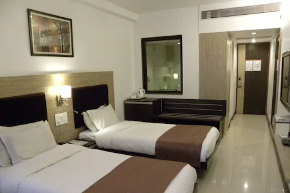 Habitación de hotel con dos camas, una mesita de noche, una lámpara, un espejo y una puerta que da a un pasillo.