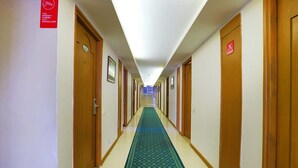 Pasillo de hotel con puertas de madera, alfombra verde y letreros de advertencia de circuito cerrado.