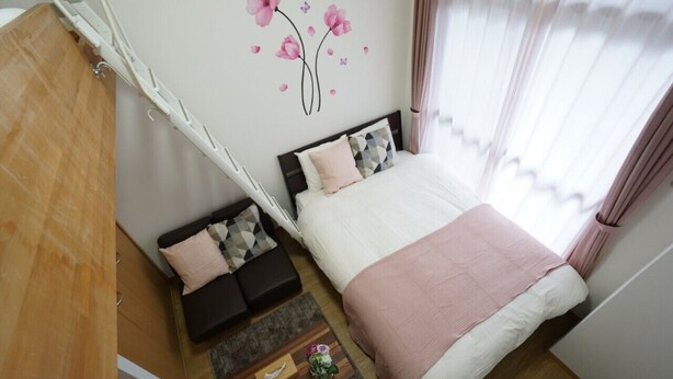 A bedroom with a bed, a sofa, a wooden wardrobe, and a wall decoration. - Apartment VR Hakuyu Motomachi Namba (Osaka)