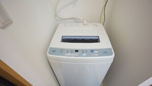 A white laundry machine in a corner of a room with a wooden floor and white walls. - Apartment VR Hakuyu Motomachi Namba (Osaka)
