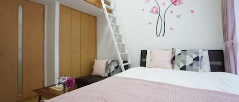 A bedroom with a bunk bed, a ladder, a desk with a vase, and a wall with floral decals.