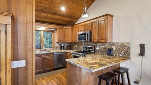 A kitchen with wooden cabinets, a granite countertop, a microwave, a stove, and two bar stools. - Meadow Ridge: Beautiful Views, Close to Eagle Lodg (Mammoth Lakes)