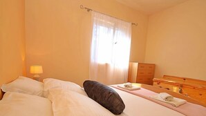 Habitación de hotel con dos camas, un aparador de madera, un espejo y una ventana con cortinas traslúcidas.