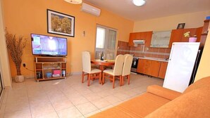 Una sala de estar con sofá, televisor, mesa de comedor con sillas y una zona de cocina con armarios y un refrigerador.