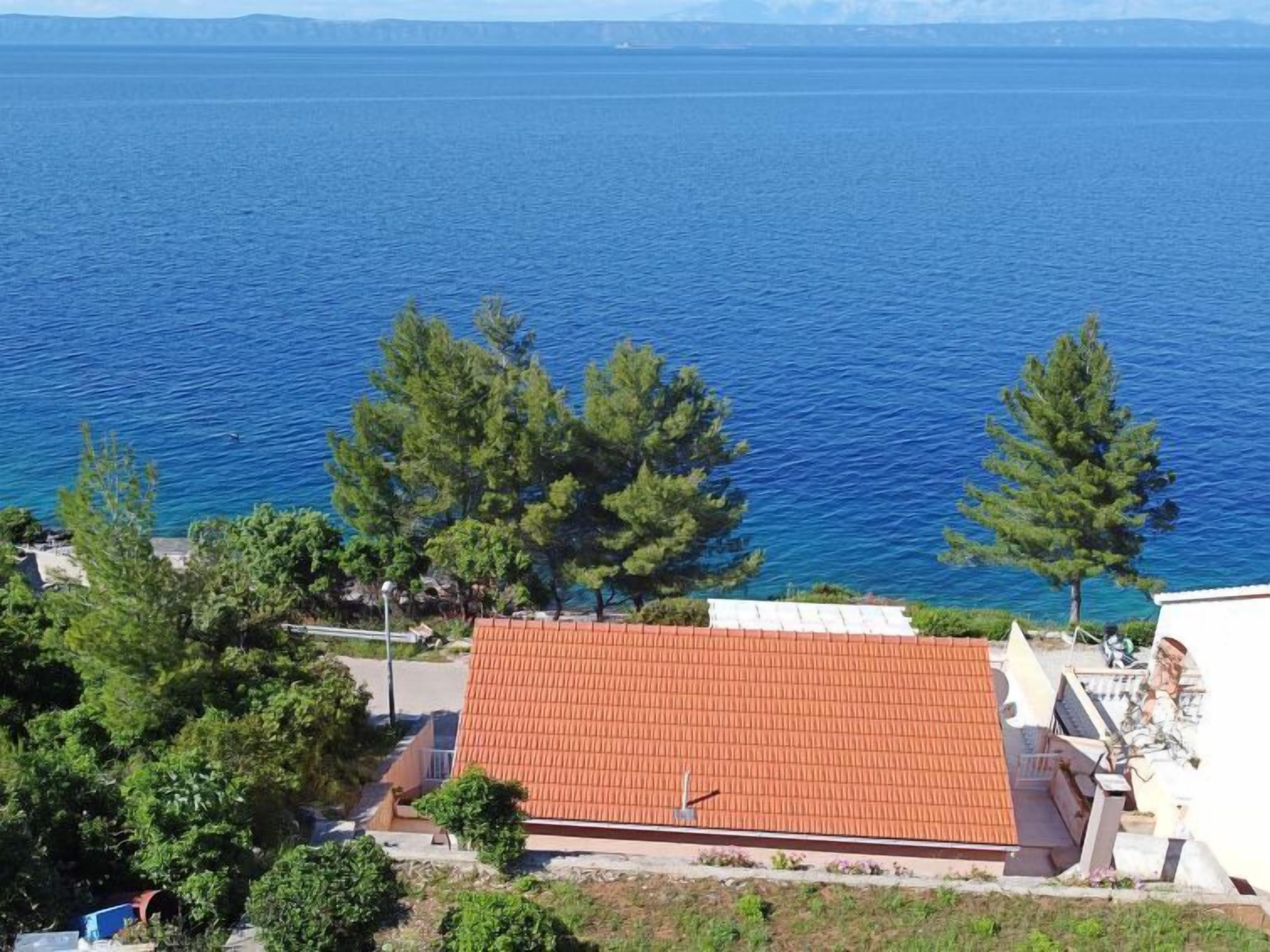 A building with a red roof, surrounded by trees and overlooking a body of water.