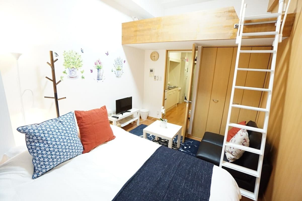 A compact hotel room with a bunk bed, a small desk, a TV, and a kitchenette.