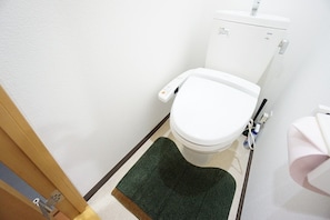 A small, white toilet with a control panel, a green mat, and a towel hanging on a rack. - Apartment Y Hakuyu Motomachi Namba (Osaka)