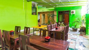 Un espace repas avec des tables et des chaises en bois, des murs verts et des plantes en pot.