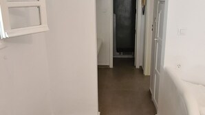 Un couloir étroit aux murs blancs et au sol marron mène à une porte.