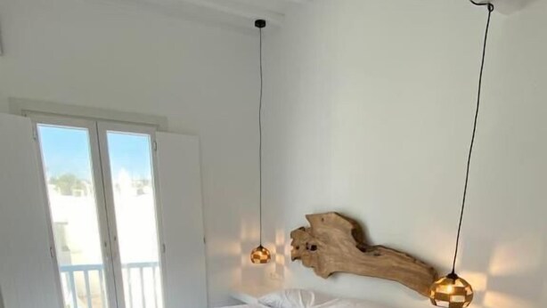 Une chambre à coucher au style minimaliste, avec un grand lit, une tête de lit en bois et deux lampes suspendues.