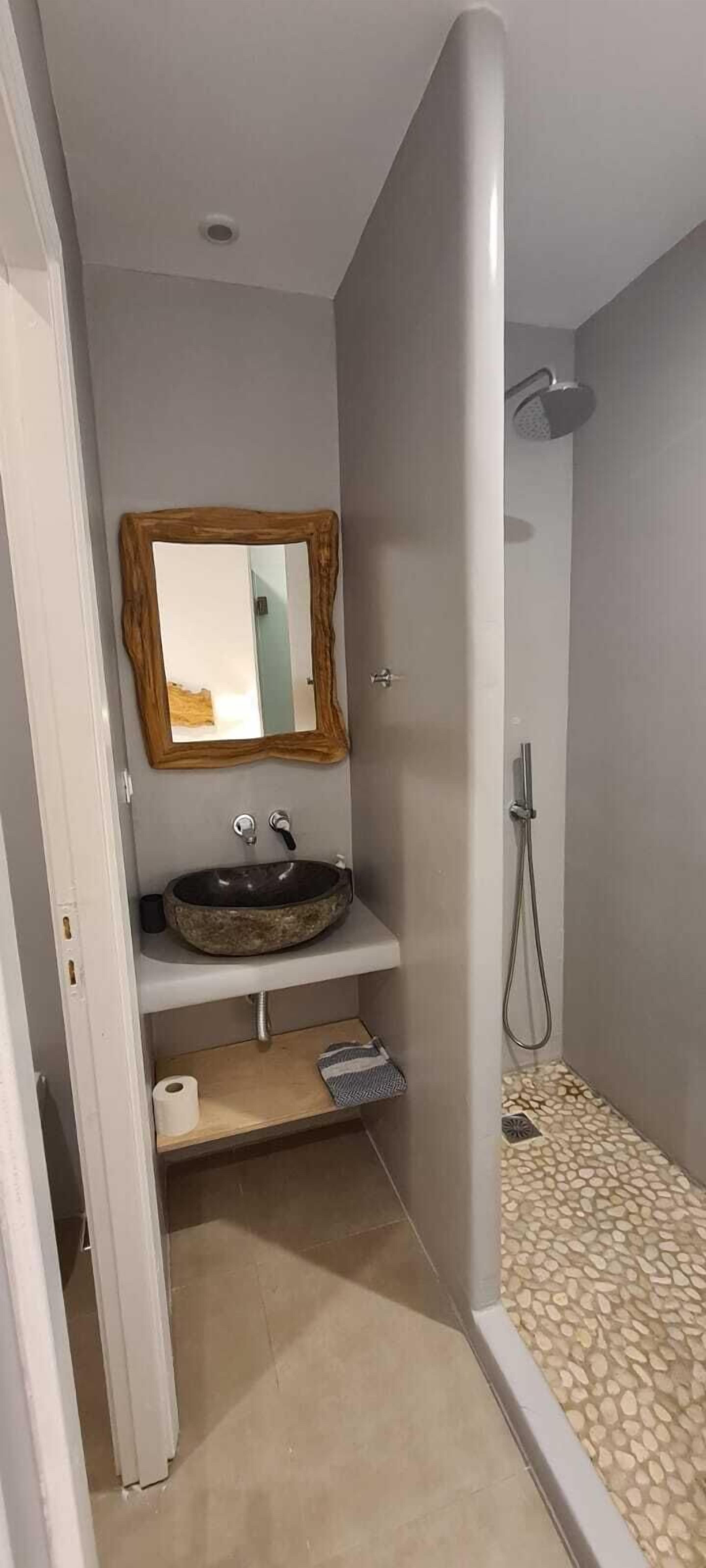 A bathroom with a stone sink, a wooden-framed mirror, a shower, and a tiled floor.