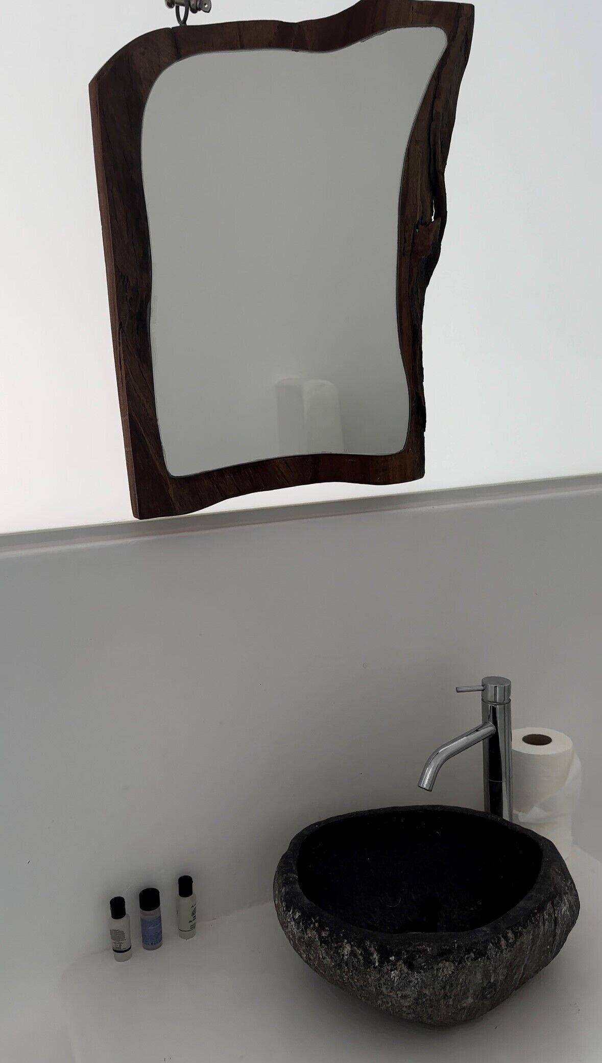 Un baño con un lavabo redondo negro, un espejo con marco de madera, un grifo y tres pequeñas botellas de jabón.