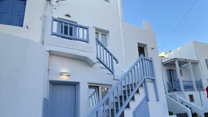 Un bâtiment blanc avec des portes et des fenêtres bleues, un escalier et une rue pavée de pierres.