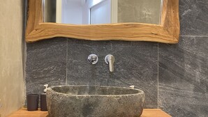 Une salle de bain avec un lavabo en pierre, un meuble-lavabo en bois et un miroir avec un cadre en bois.