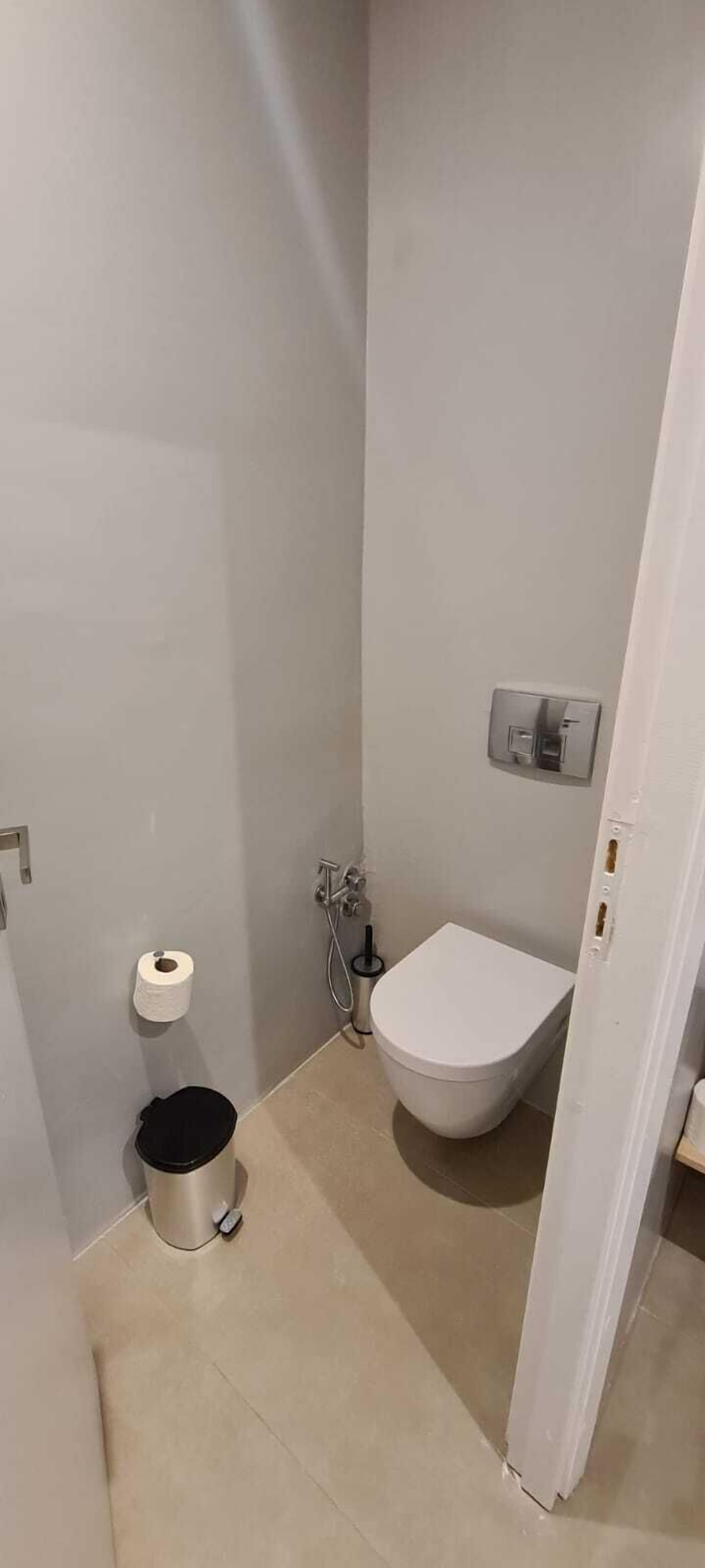 A small, compact bathroom with a toilet, a trash can, and a paper towel dispenser.