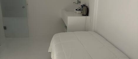 A bedroom with a bed, a bedside table, a mirror, and a door.