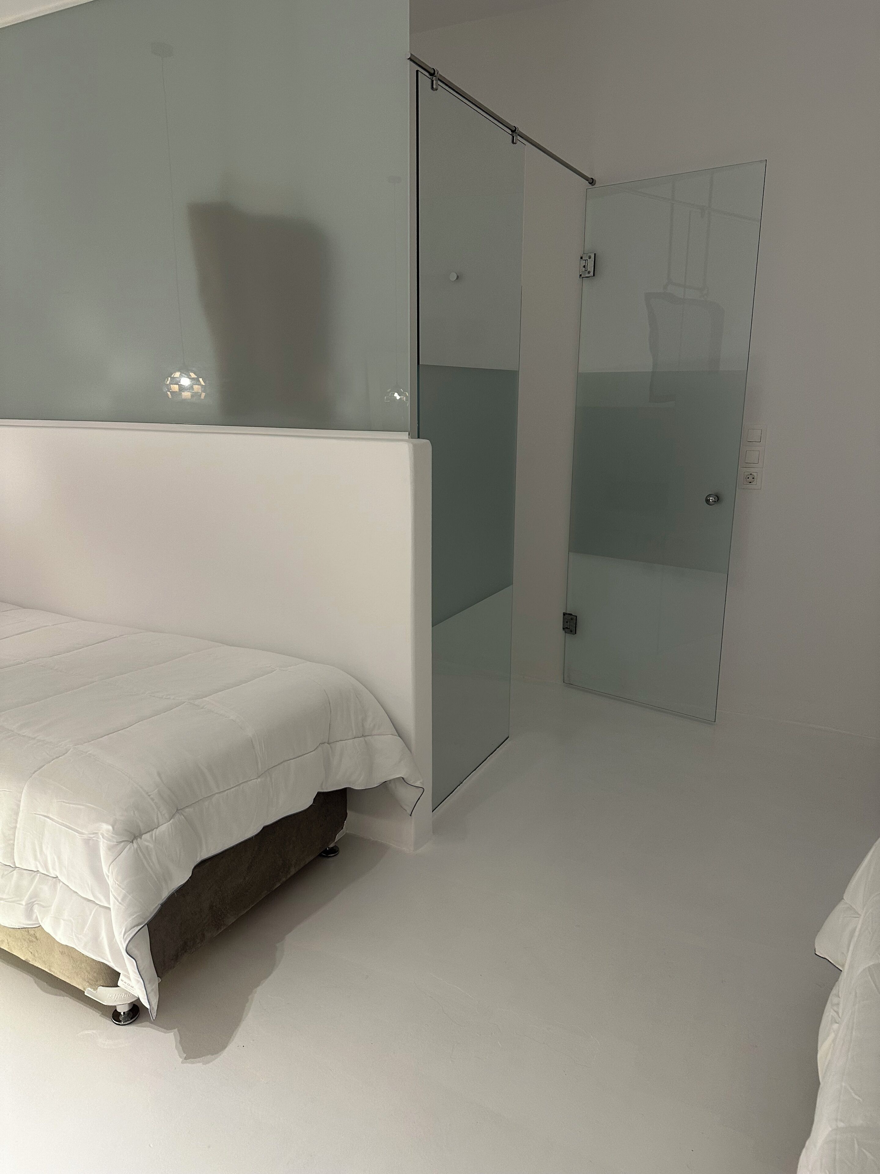 A modern bedroom with a bed, a glass door, and a white wall.