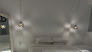 Une chambre moderne avec un grand lit, deux lampes suspendues, une table de chevet et un miroir.