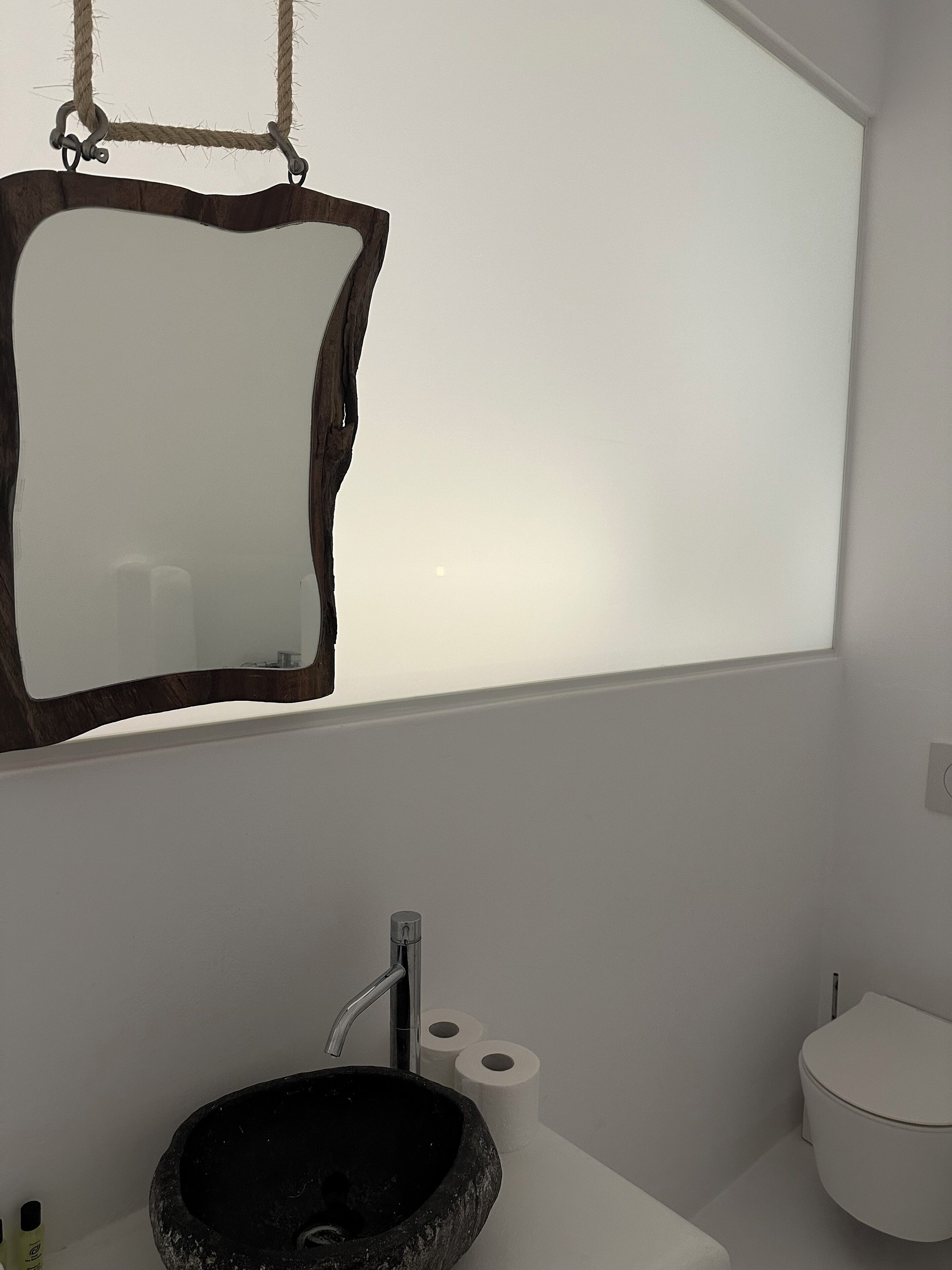 A bathroom with a stone sink, a white toilet, and a mirror with a wooden frame.