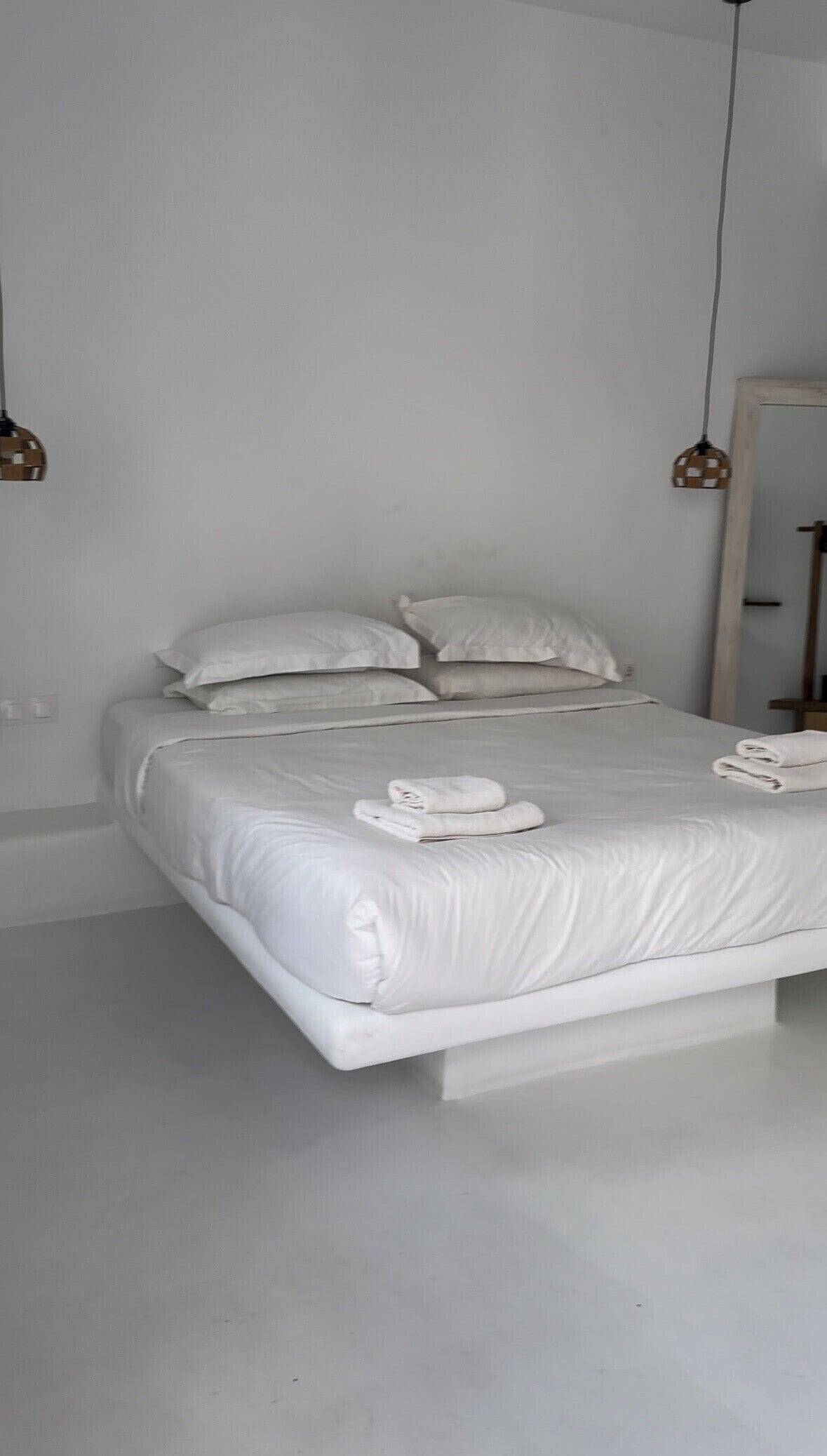 A modern, minimalist bedroom with a large bed, white linens, and two pendant lights.