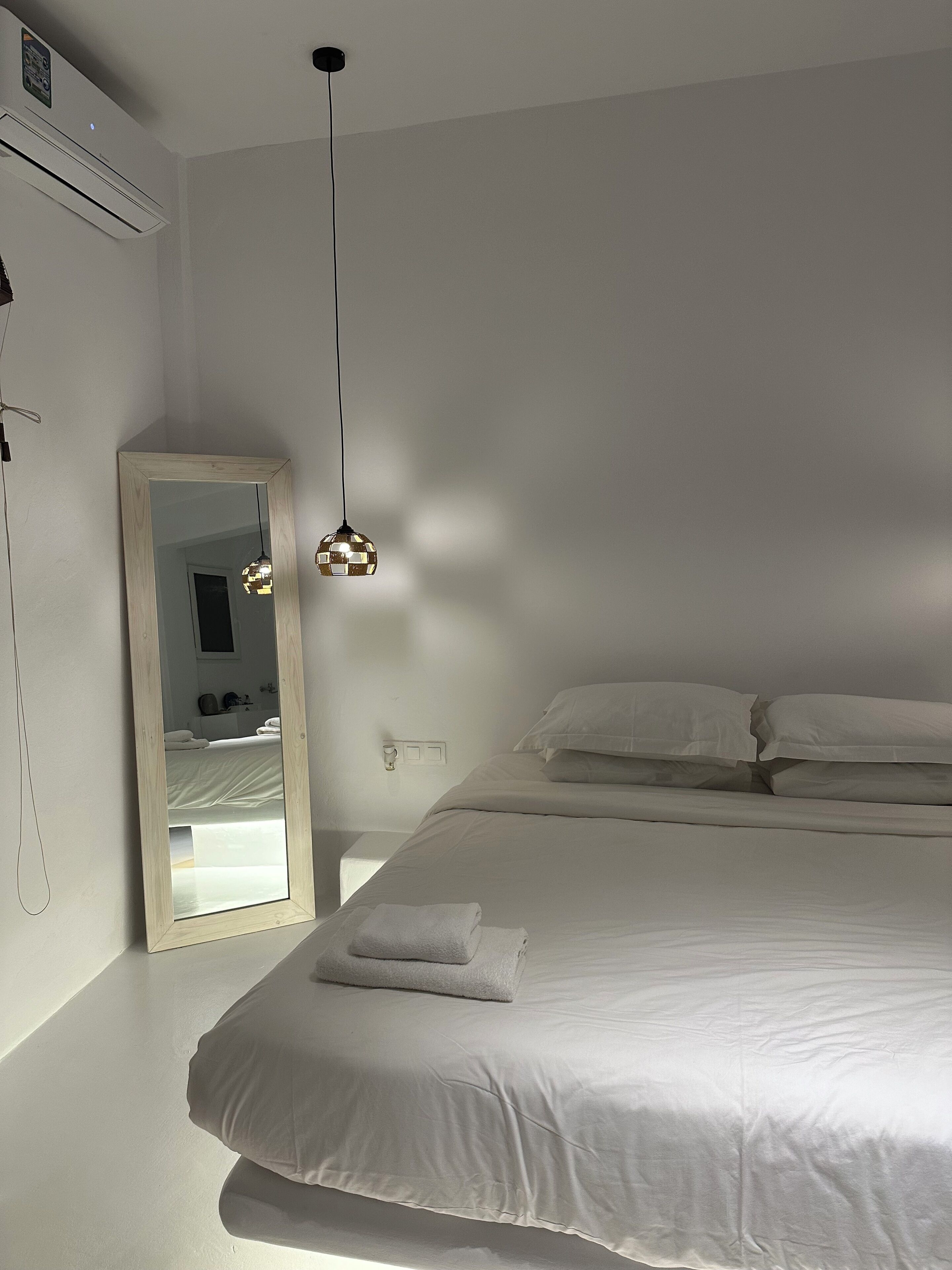 A bedroom with a large bed, a bedside table, a mirror, and a hanging light fixture.