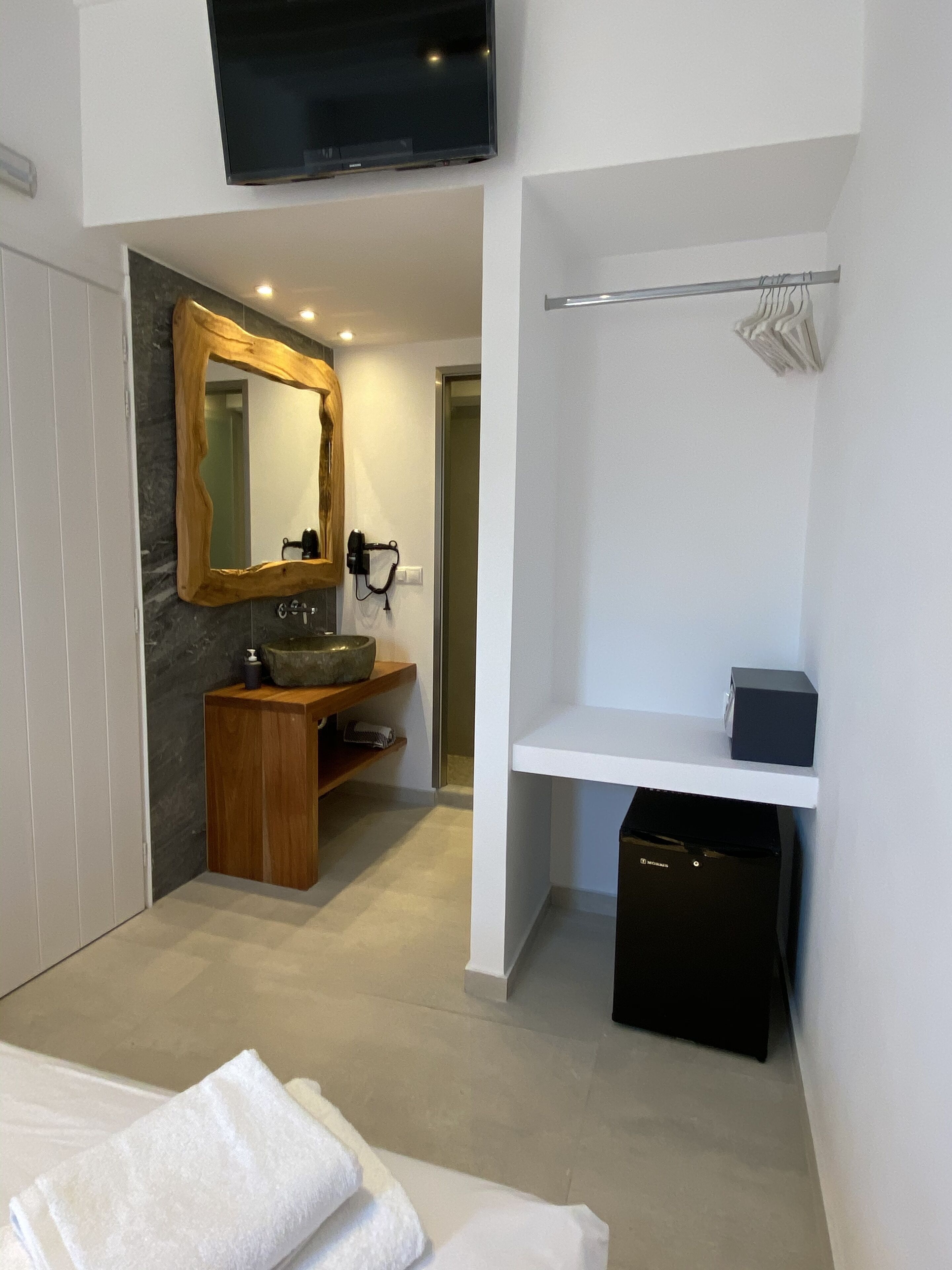 A modern bathroom with a wooden vanity, a large mirror, a black trash bin, and a white shelf.