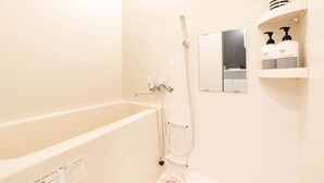 A bathroom with a bathtub, a handheld showerhead, a wall-mounted mirror, and shelves with shampoo and conditioner bottles. - Apartment Y Legendoal Nipponbashi (Osaka)