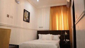 A hotel room with a bed, a nightstand, a lamp, and a painting on the wall. - Greenland Suites (Lagos)