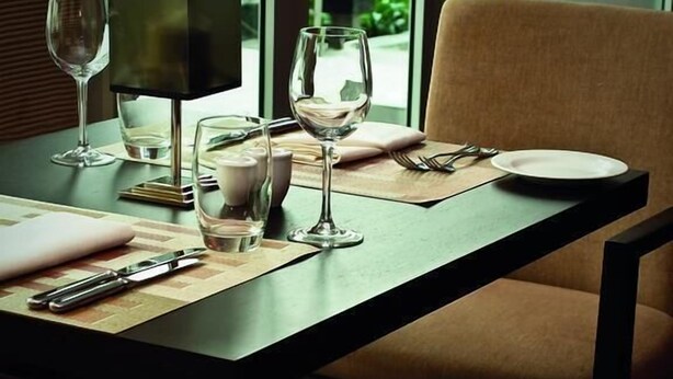 A dining table set with wine glasses, plates, and cutlery, with a chair and a lamp on the table. - Greenland Suites (Lagos)