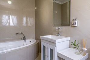 A modern bathroom with a bathtub, a sink, and a mirror. There are two bottles of hand soap on the wall. - Auriol's Guesthouse (Cape Town)