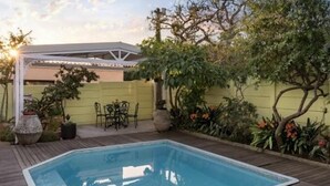 Una piscina rectangular con cubierta de madera, rodeada de plantas en macetas y una valla amarilla.