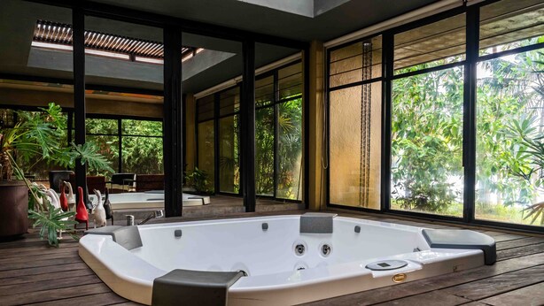 Un jacuzzi en una terraza de madera con amplios ventanales que dan a un jardín exuberante.