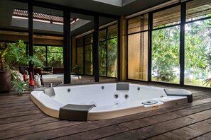 Un bain à remous sur une terrasse en bois, avec de grandes fenêtres donnant sur un jardin luxuriant.