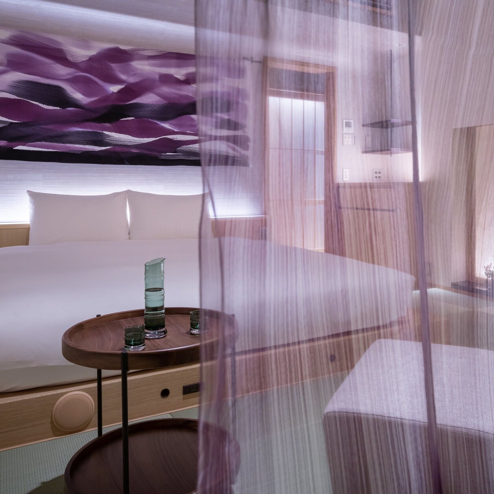 Une chambre d’hôtel avec un lit, une table de chevet et un mur orné d’un motif abstrait violet.