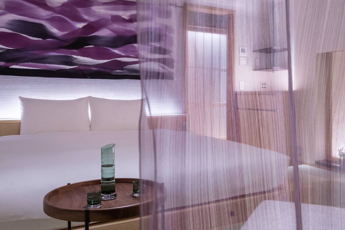 Une chambre d’hôtel avec un lit, une table de chevet et un mur orné d’un motif abstrait violet.