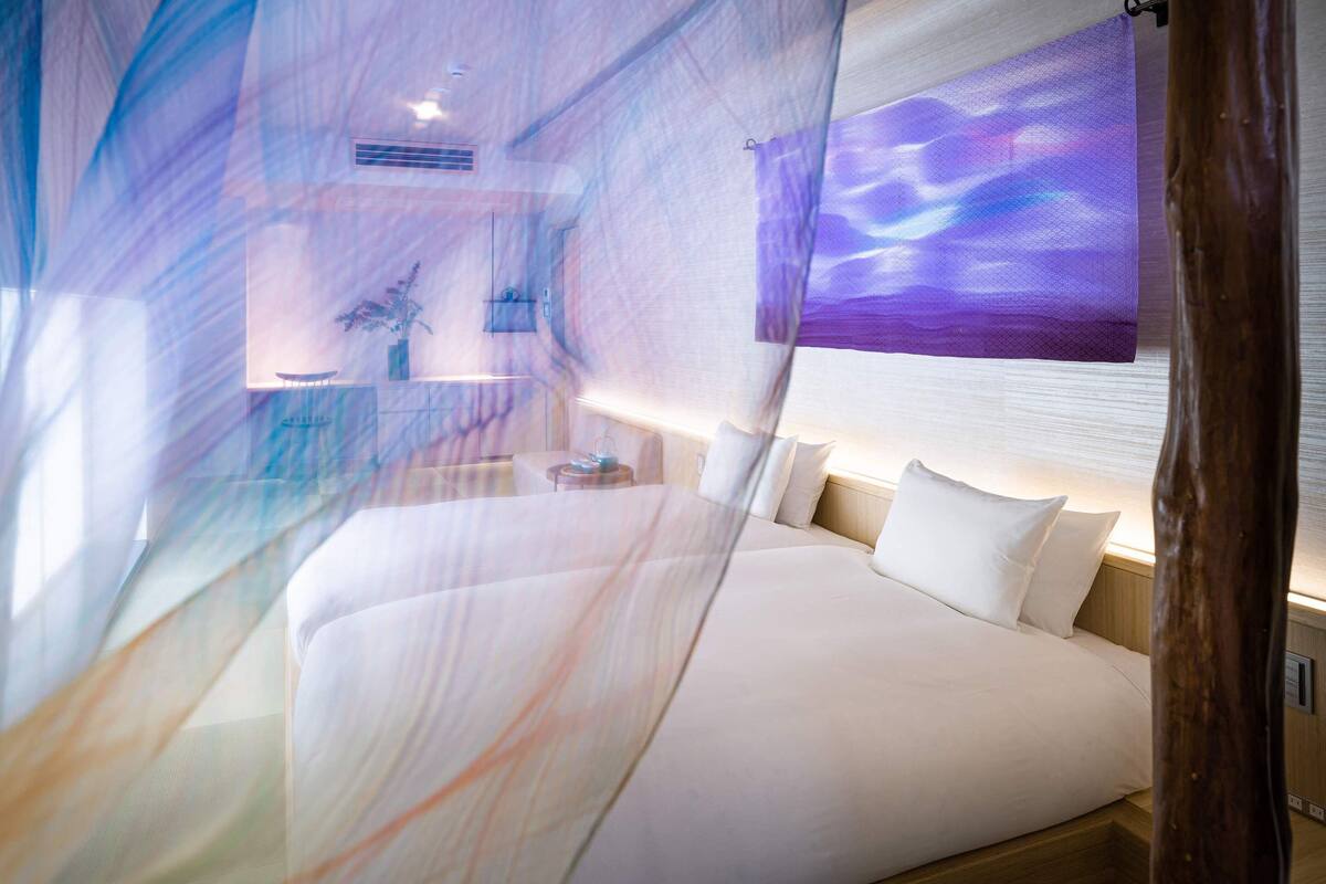 Une chambre d’hôtel moderne dotée d’un grand lit, de tables de chevet, d’une petite table, d’une fenêtre offrant une vue et d’un téléviseur fixé au mur.