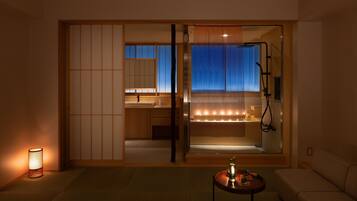 Een moderne hotelkamer met een schuifdeur naar een badkamer, een tafeltje met een lamp en een bank.