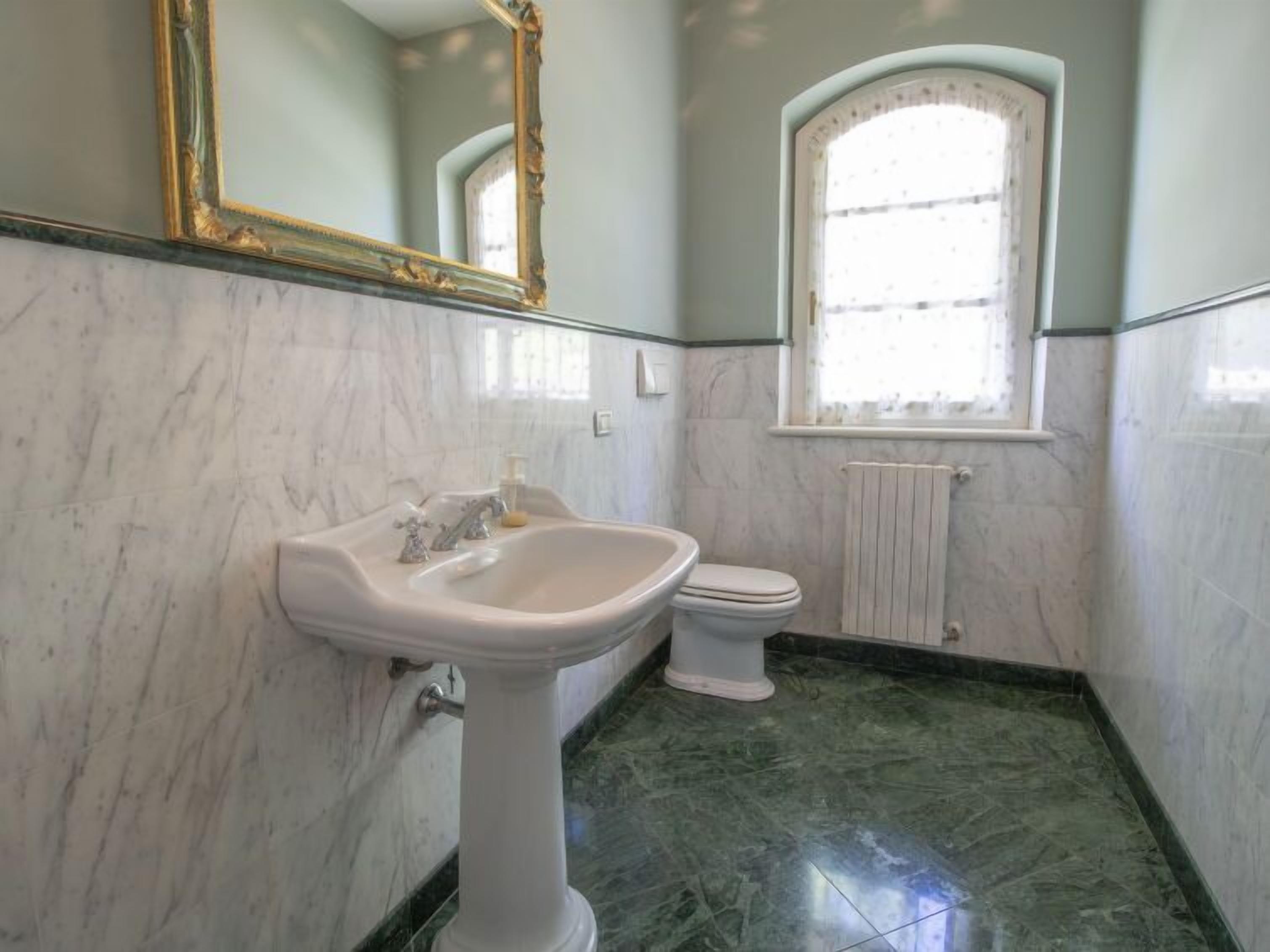 Een badkamer met een marmeren wastafel, toilet en een raam met een witte handdoekradiator.