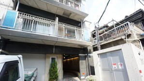 A multi-story residential building with a covered entrance, a small garden area with potted plants, and a white van parked in front. - Apartment Y Mell Theater Resort (Osaka)
