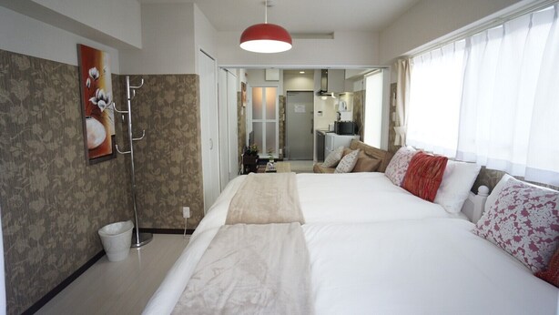 A hotel room with a large bed, a red pendant light, a bathroom with a shower, and a kitchenette in the background. - Apartment Y Mell Theater Resort (Osaka)