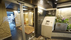 A hotel lobby with a reception desk, a glass door entrance, a patterned rug, and a stone floor. - Apartment Y Mell Theater Resort (Osaka)